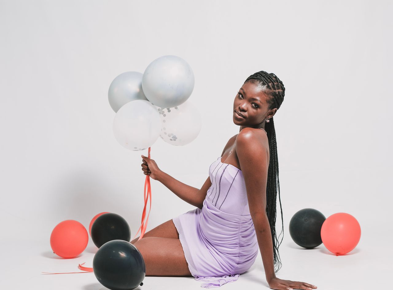 creative-03 A stylish woman poses with colorful balloons against a white background, embodying celebration and grace.
